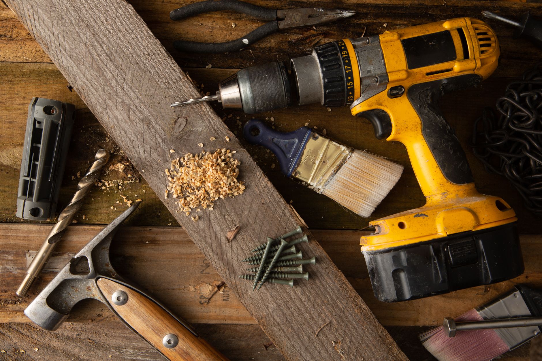 A close-up of various tools including a drill, hammer, and paintbrush on a wooden workbench. — Going about the asbestos surve