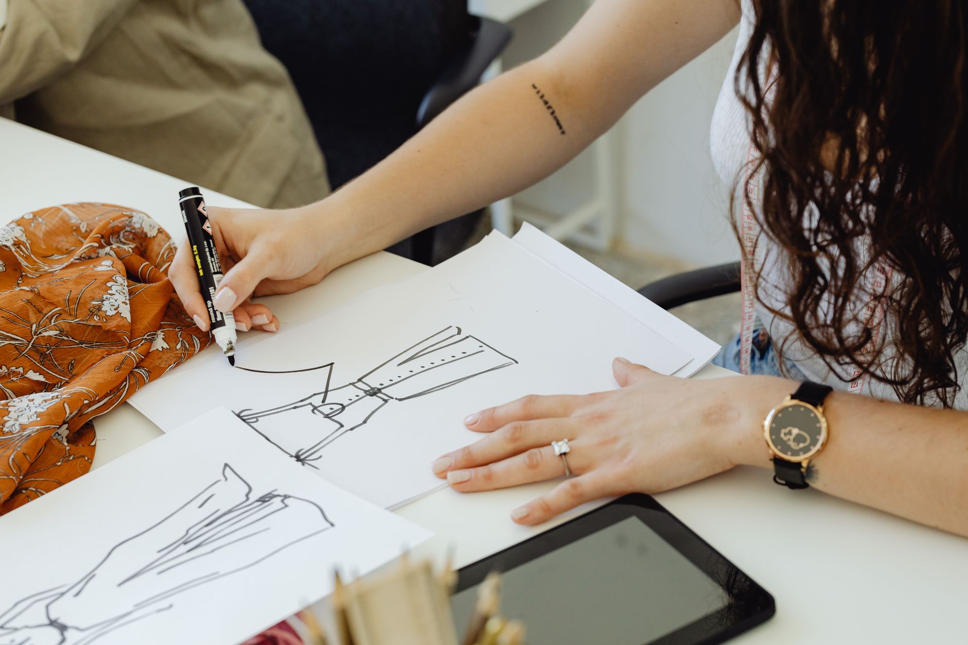 Fashion designer sketching dress ideas at a desk with fabric and sketches. — In this modern age of the Internet, expand your