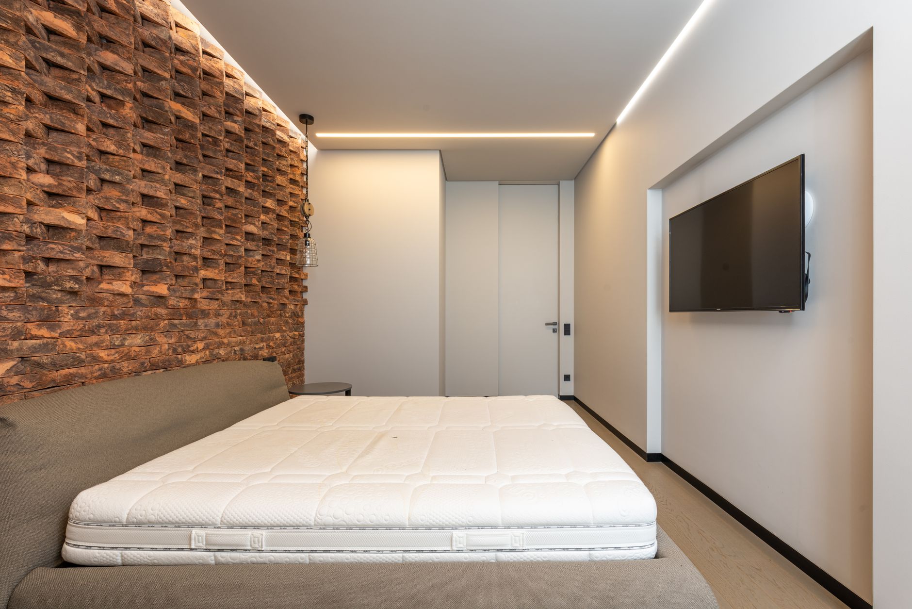 Comfortable be with soft mattress in stylish minimalist bedroom with modern TV and creative brick wall — Mediterranean Interi