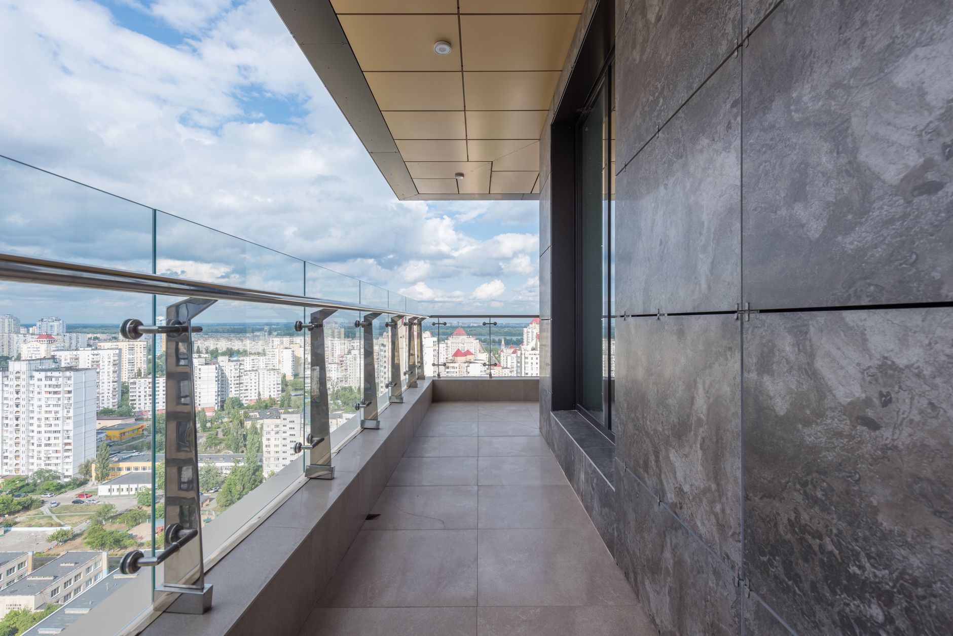 Spacious terrace with glass barrier and metal railings of contemporary apartment in multistory building against cloudy blue s