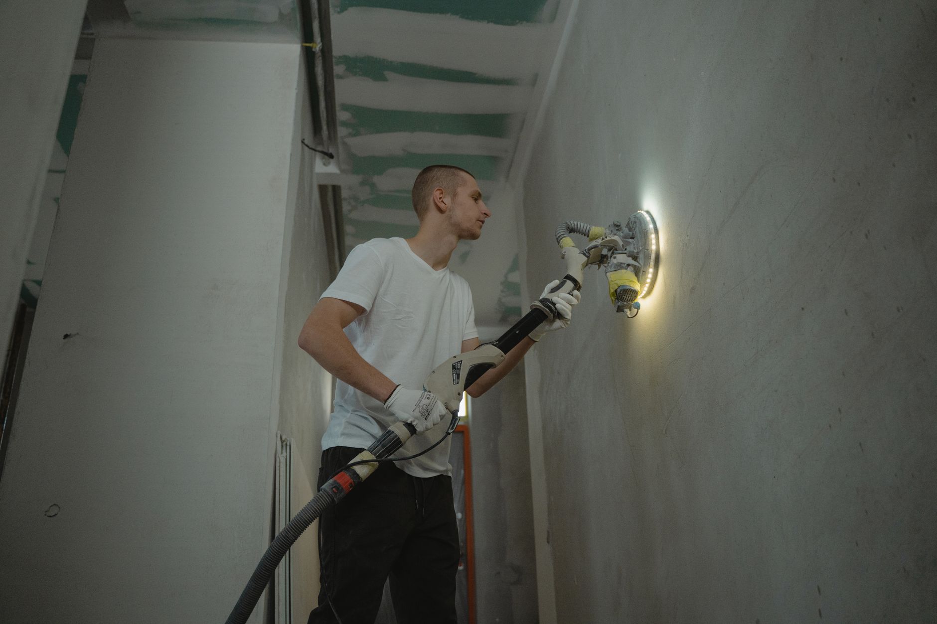 A man sanding an interior wall with an automatic sanding tool during renovation work indoors. — Simple Home Upgrades That Mak
