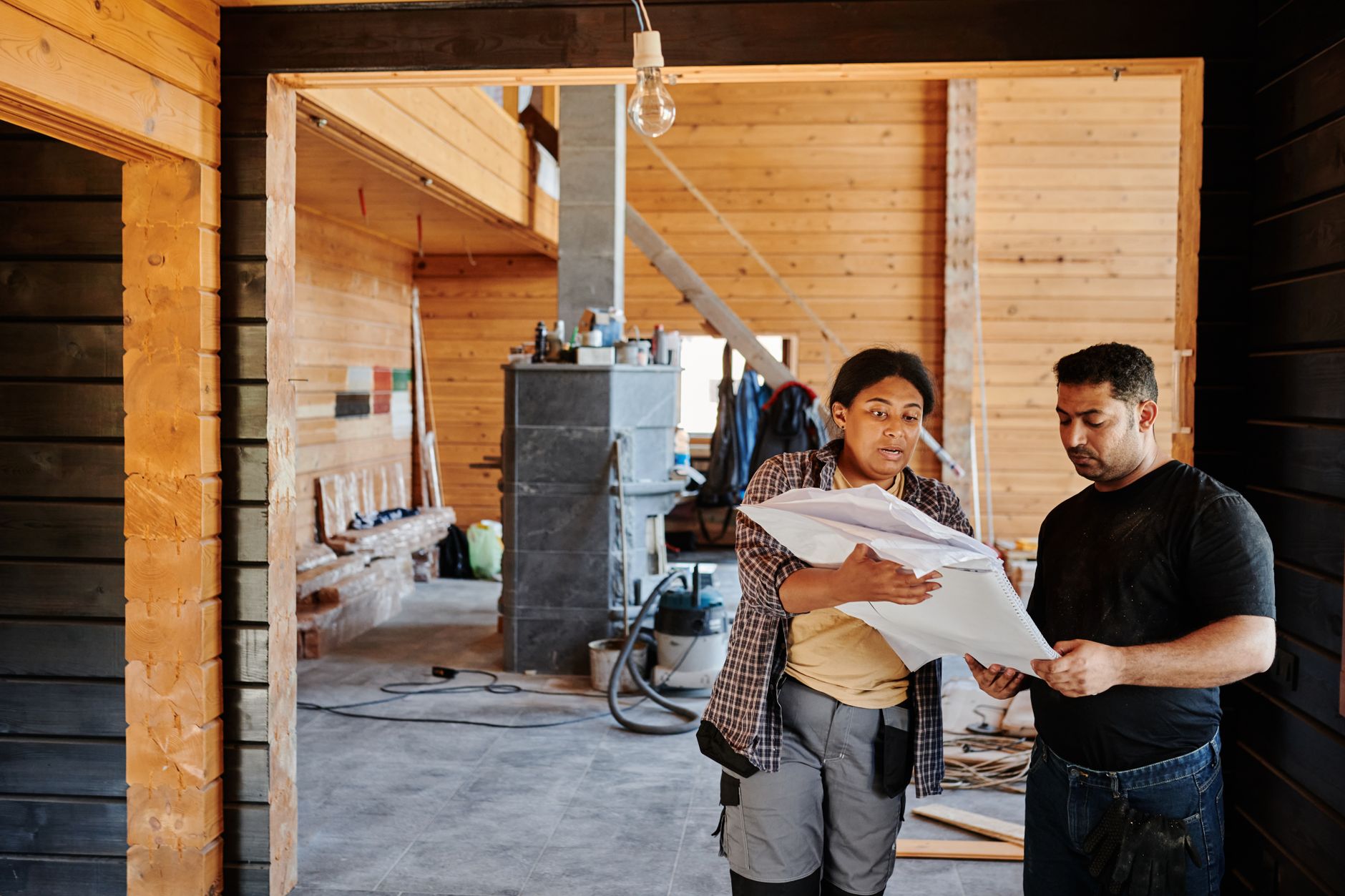 Construction workers reviewing blueprints indoors at a renovation site with wooden walls. — Tackling Package Homes: Here's Wh