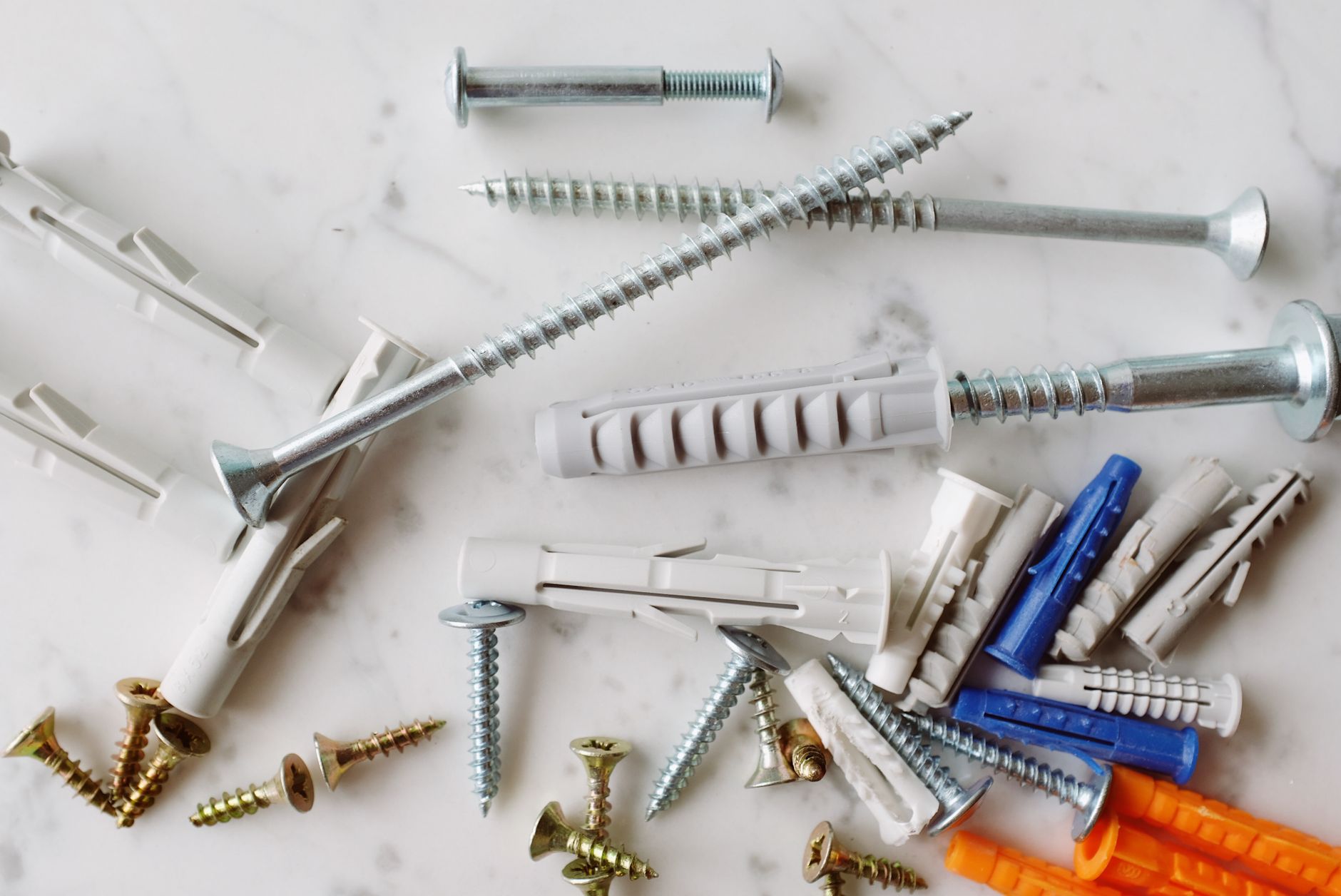 Set of various multicolored plastic dowels with metal screws of different sizes placed on white marble table in modern worksh